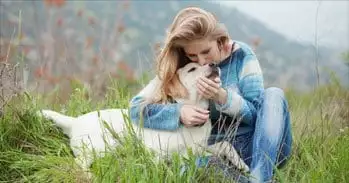 A woman cuddling with her dog in a meadow.