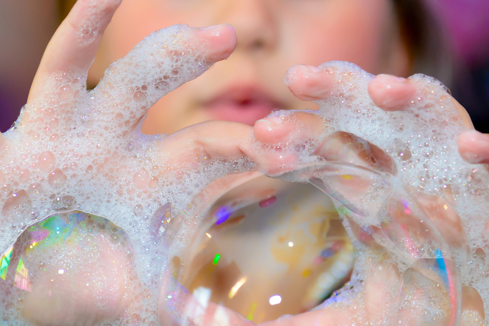 close up of child blowing bubbles using soapy hands