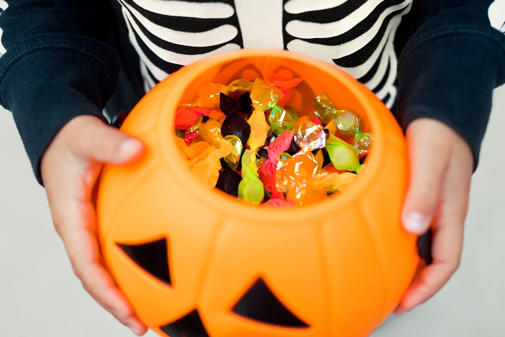 kid's hands holding pumpkin bucket filled with candy
