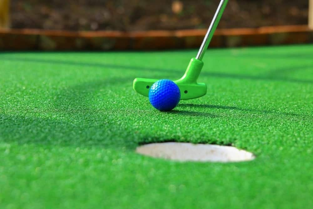 A blue golf ball rolls near hole on mini golf course