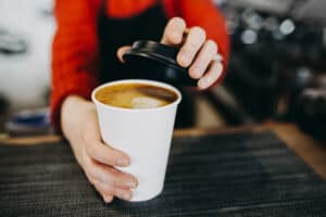 barista putting lid on white to-go coffee cup