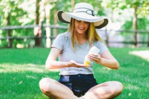 young woman applying sunscreen while wearing wide-brimmed hat